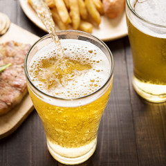 Beer being poured into glass with steak and french fries on wood