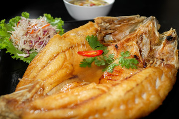 fried fish with fresh herbs and sweet spicy sauce on plate in bl