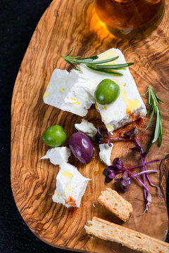 Feta cheese on wooden board with olives and oil