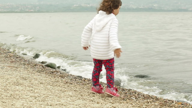 little girl sitting on the beach and throwing stones 