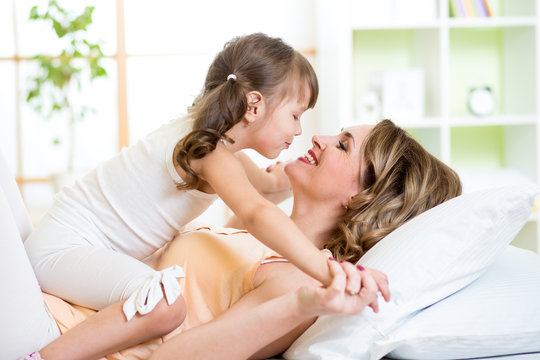 Mom and child daughter embracing and kissing in bed