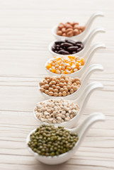Different kinds of bean seeds, lentil, peas in dish on wooden ta
