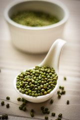 Raw mung beans in ceramic spoon over white wooden background