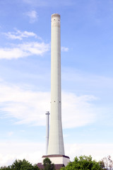 Fototapeta na wymiar a high concrete chimney with white smoke clouds blue sky