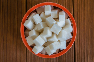 Sugar in red bowl on dark wooden background. 
