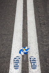 Fototapeta premium Beach slippers with pinwheel lying on grey asphalt