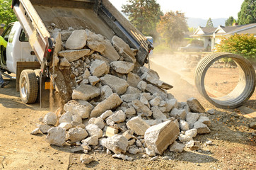 A small dump truck dumps concrete pieces 