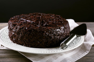 Delicious chocolate cake in plate on wooden table on dark background