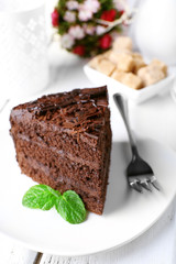 Piece of delicious chocolate cake with mint in plate with fork on color wooden table background