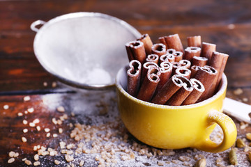 Cinnamon sticks in cup with sugar on wooden table background