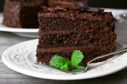 Delicious chocolate cake in white plate with mint on wooden table background, closeup