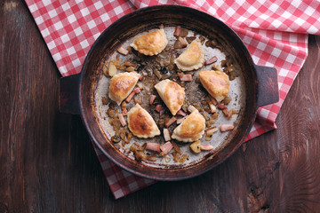 Fried dumplings with onion and bacon in frying pan, on wooden table background