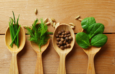 Wooden spoons with fresh herbs and spices on wooden background