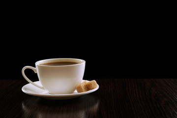 Cup of coffee with lump sugar on wooden table, on dark background