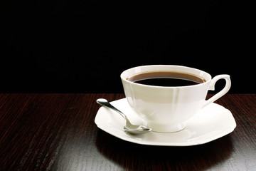 Cup of coffee on wooden table, on dark background