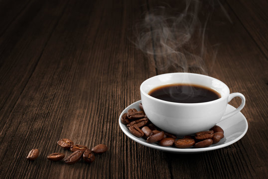 Cup of hot coffee on a wooden table. Coffee beans. Steam.
