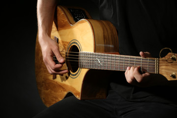 Plakat Young man playing on acoustic guitar on dark background