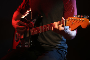 Obraz na płótnie Canvas Young man playing on electric guitar on dark background