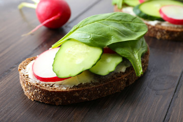 Delicious sandwiches with vegetables and greens on wooden table