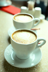 Cups of cappuccino with heart on foam on table in cafe