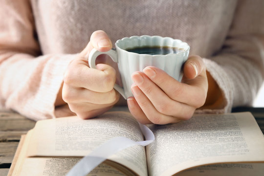 Woman holding cup of coffee and read the book, close up