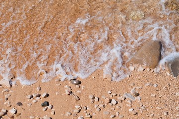 Sandy beach with pebbles and wave as background