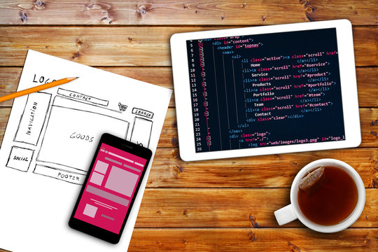 website wireframe sketch and programming code on digital tablet