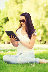 smiling young girl with tablet pc sitting on grass