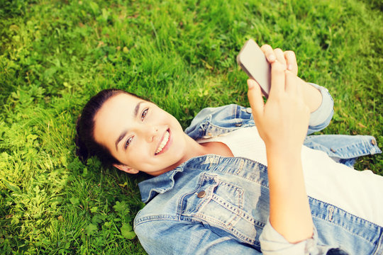 smiling young girl with smartphone lying on grass