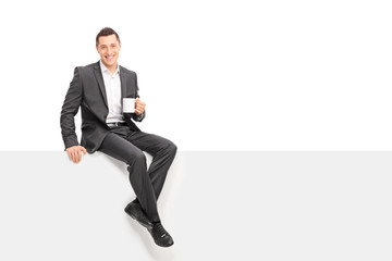 Businessman holding a cup of coffee seated on panel