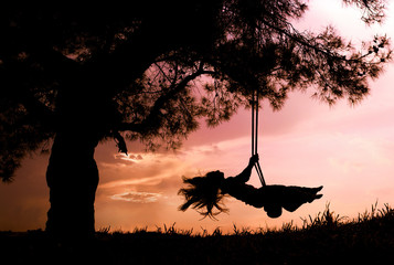 silhouette of happy young woman on a swing with sunset