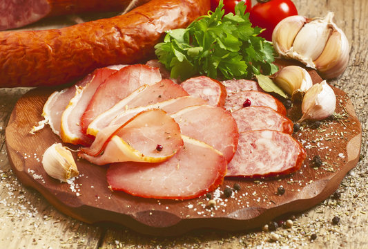 Slices of smoked ham and sausages on a cutting board in a rustic