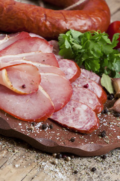 Slices of smoked ham and sausages on a cutting board in a rustic