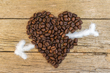Coffee beans heart stabbed by white sugar on wooden background