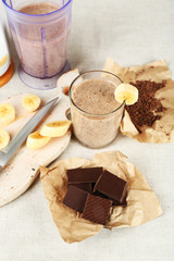 Sliced banana on cutting board and chopped chocolate, on wooden background