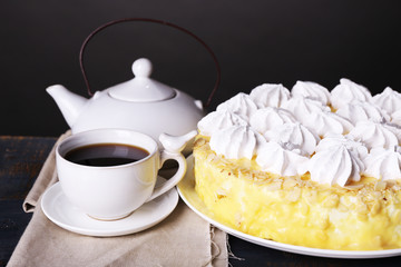 Tasty homemade meringue cake and cup of tea on wooden table, on grey background