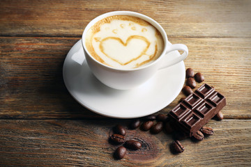 Cup of coffee latte art with grains and chocolate on wooden background