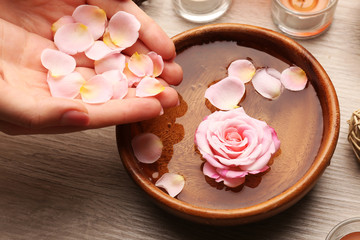 Female hands and bowl of spa water with flowers, closeup