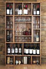 Shelving with wine bottles with glasses on wooden wall background