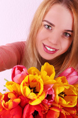 Fototapeta premium Portrait of young woman with beautiful bouquet of tulips on wallpaper background