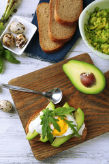 Tasty sandwich with egg, avocado and arugula on wooden background