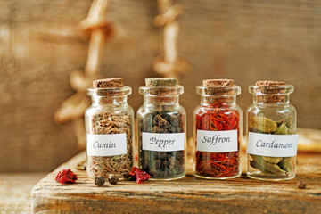 Assortment of spices in glass bottles on cutting board, on wooden background
