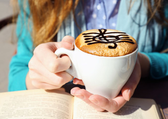 Hands holding cup of cappuccino with treble clef on foam