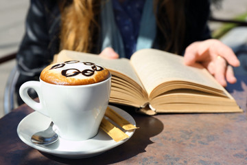 Woman reading book and cup of cappuccino in cafe, outdoors