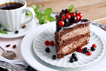 Delicious chocolate cake with berries and cup of coffee on table close up
