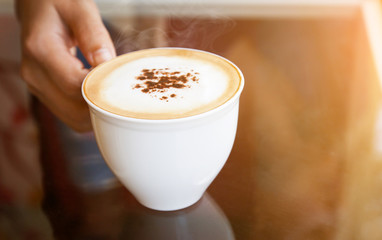 A woman's hand holding a cup of hot coffee in the morning.