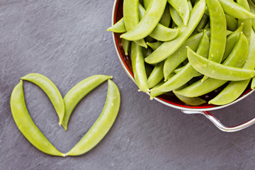 Green peas in red colander and single one on the side