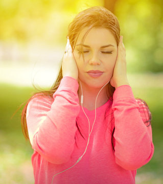 Female student girl outside in park listening to music on headph