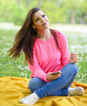 Female student girl outside in park listening to music on headph