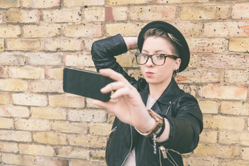 Hipster woman taking a selfie against brick wall in London.